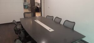 Professional boardroom table with seating and presentation screen setup in a furnished office rental in Okhla.