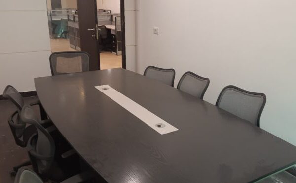 Professional boardroom table with seating and presentation screen setup in a furnished office rental in Okhla.